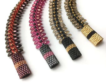 May include: Four beaded necklaces with different color combinations. The necklaces are made with small, round beads in shades of brown, pink, and gray. Each necklace has a black and gold beaded end cap.