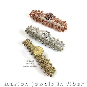 May include: Three crocheted bracelets with different colored beads and metal button accents. The bracelets are in gold, silver, and copper tones. The buttons feature a flower, a heart, and a flower design.