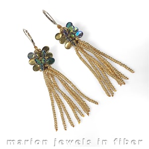 Puede incluir: Pendientes de cuentas doradas con un racimo de cuentas iridiscentes verdes y azules en la parte superior. Las cuentas están dispuestas en forma de flor.