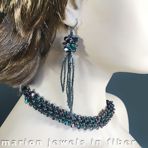 May include: A dark green and black beaded necklace and earrings set. The necklace is a choker style and the earrings are long and dangle. The beads are iridescent and have a subtle shimmer.