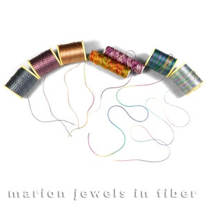 May include: A collection of colourful spools of thread with their ends unraveled and spread out on a white surface. The spools are arranged in a semi-circle shape, with the ends of the thread forming a pattern of loops and swirls.