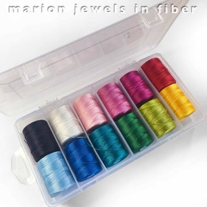 May include: A clear plastic storage box with 10 spools of colorful thread. The spools are arranged in a rainbow pattern, starting with black and ending with yellow.