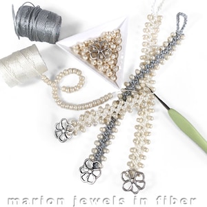 May include: Three beaded bracelets with silver flower charms, a hook, and spools of white and gray thread. The beads are white and gray.
