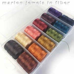 May include: A clear plastic storage box filled with 10 spools of colorful embroidery floss. The floss colors are purple, dark brown, teal, green, gold, orange, brown, black, and cream.