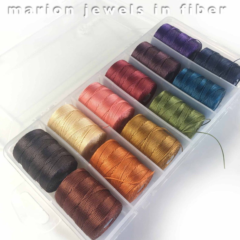 May include: A clear plastic storage box filled with 10 spools of colorful embroidery floss. The floss colors are purple, dark brown, teal, green, gold, orange, brown, black, and cream.