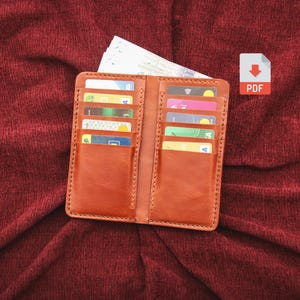 Puede incluir: Una cartera de cuero color canela con múltiples ranuras verticales para tarjetas en ambos lados, llena de varias tarjetas de crédito coloridas y un documento de papel blanco en el bolsillo superior, con un icono PDF en la esquina superior derecha.