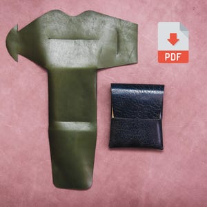 May include: An overhead shot displays two leather items and a PDF icon on a pink background. One item is a dark green, T-shaped piece. The other is a small, black, rectangular pouch. The PDF icon has a red arrow.