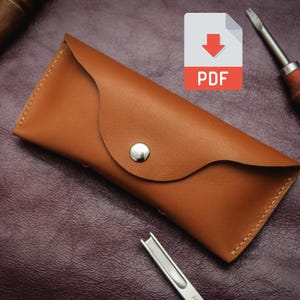 May include: A handcrafted, brown leather glasses case with a snap closure. The case is surrounded by leatherworking tools, including screwdrivers and a wooden awl. A PDF icon is in the upper right corner.