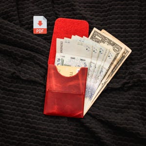 May include: A red leather card holder wallet containing several paper banknotes and a single credit card. The wallet features a vertical orientation with a flap closure and a smooth, slightly marbled texture on the exterior surface.