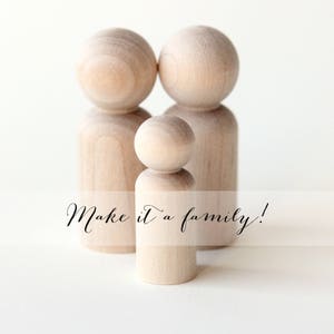 Puede incluir: Tres mu&ntilde;ecos de madera sin pintar, que representan a una familia, se alzan sobre un fondo blanco. Los mu&ntilde;ecos tienen cabezas redondeadas y cuerpos cil&iacute;ndricos. El texto "Make it a family!" est&aacute; escrito en la parte inferior.