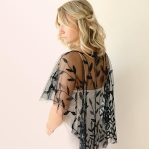 May include: Black sheer lace shawl with a leaf pattern. The shawl is draped over a person's shoulders.