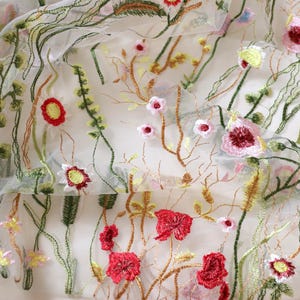 May include: White sheer fabric with embroidered floral designs in shades of red, pink, yellow, and green.