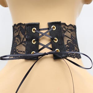 May include: Black lace choker with a satin ribbon tie and gold eyelets. The choker is adjustable and can be worn as a statement piece or a subtle accessory.