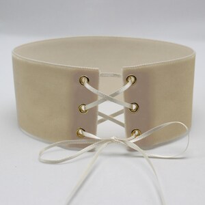 May include: A beige velvet choker with white satin ribbon laces and gold metal eyelets.