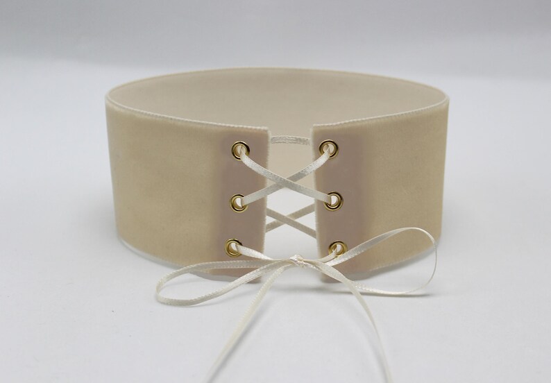 May include: A beige velvet choker with white satin ribbon laces and gold metal eyelets.