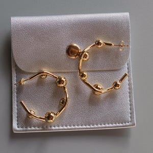 Op de afbeelding: Twee gouden creolen met een parelmoer ontwerp. De oorbellen worden getoond op een witte achtergrond.