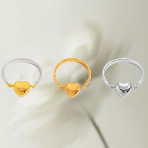 May include: Three rings with heart-shaped centerpieces. One ring is gold, another is silver, and the third is gold with a silver band. The heart-shaped centerpieces are connected to the bands with small connectors.
