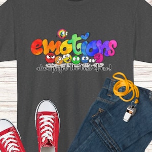 May include: Dark grey t-shirt featuring the word "emotions" in colourful lettering and expressive faces. The text "always get the best of me!" is below. Red trainers and blue jeans are also in the image.