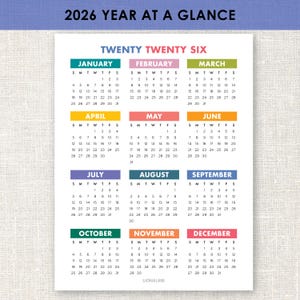 Può includere: Un calendario del 2026 con una panoramica dell'anno, su sfondo bianco. Ogni mese ha un'intestazione di colore diverso. Il testo "Twenty Twenty Six" è in alto. Il calendario è di Lion & Lane.