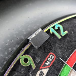 Op de afbeelding: Close-up van een dartbord met een zwart "Precise 180" segment en het nummer "12" zichtbaar. Het dartbord heeft een zwart, groen en rood kleurenschema.