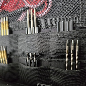 Könnte beinhalten: Ein schwarzer Dartkoffer mit mehreren Fächern zur Aufbewahrung von Darts. Der Koffer hat ein Netzfach oben und ist aus strapazierfähigem Stoff gefertigt.