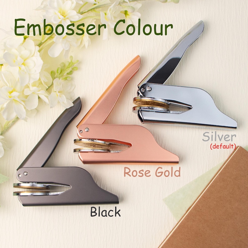 May include: Three embosser stamps in different colors: silver, rose gold, and black. The stamps are made of metal and have a round design. The text "Embosser Colour" is at the top of the image. The text "Silver (default)" is below the silver stamp, "Rose Gold" is below the rose gold stamp, and "Black" is below the black stamp.