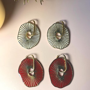 Peut inclure: Quatre paires de boucles d'oreilles. Deux paires sont blanches avec des lignes radiales noires, et deux paires sont rouges avec des lignes radiales dorées. Chaque boucle d'oreille a un anneau doré.