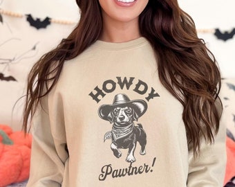 May include: A tan sweatshirt with a black and white illustration of a dog wearing a cowboy hat and bandana. The text "Howdy Pawrtner!" is printed below the dog.