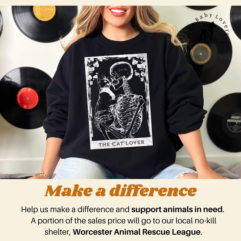 Puede incluir: Sudadera negra con un gr&aacute;fico blanco de un esqueleto sosteniendo un gato, con el texto "THE CAT LOVER". La imagen tambi&eacute;n incluye el texto "Make a difference". Parte de la colecci&oacute;n "Baby Lovers".