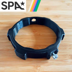May include: A black plastic ring with a screw on the side. The ring has a textured surface and a small hole in the top.