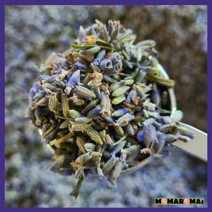 May include: A close-up of a metal spoon filled with dried lavender buds. The lavender is a mix of purple and green hues.