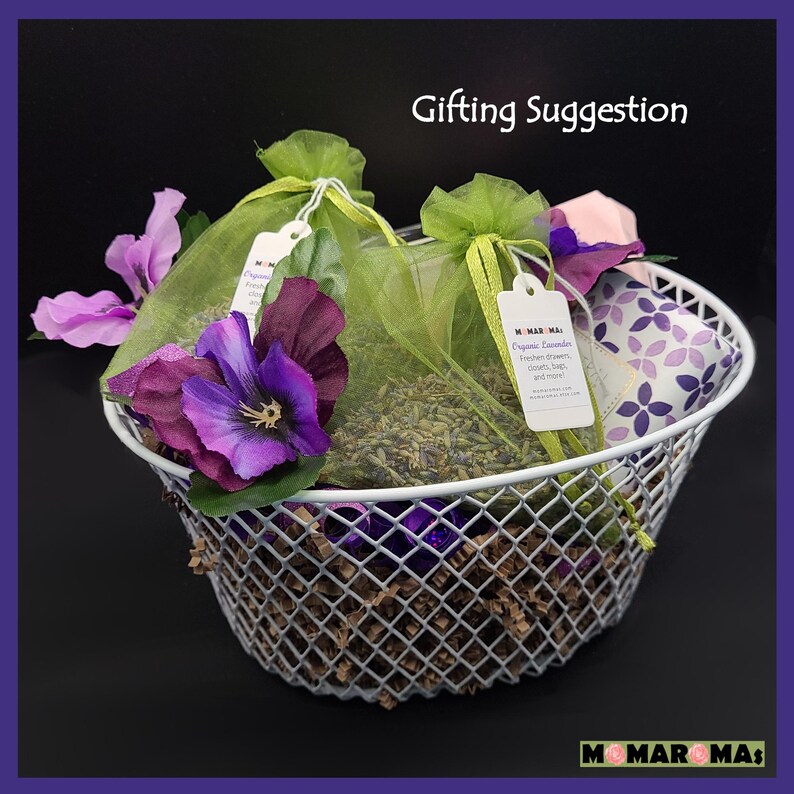 May include: A white wire basket filled with lavender sachets, purple flowers, and a small lavender-patterned pouch. The label on the sachet reads "Organic Lavender Freshen drawers, closets, bags, and more."