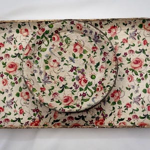 May include: A rectangular tray and a round plate with a floral pattern. The design features pink roses, purple flowers, and green leaves on a cream background. The tray and plate have a gold trim.