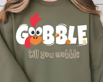 Może przedstawiać: Zielony sweter z białym nadrukiem indyka z tekstem "Gobble till you wobble" w kolorze białym.