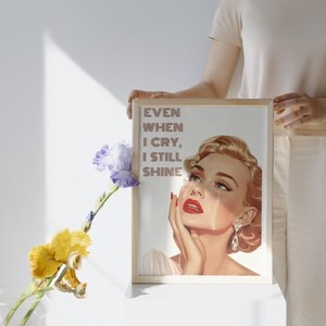 May include: A vintage-style illustration of a woman with red lipstick and tears running down her cheeks. The text "EVEN WHEN I CRY, I STILL SHINE" is printed in pink on a white background.