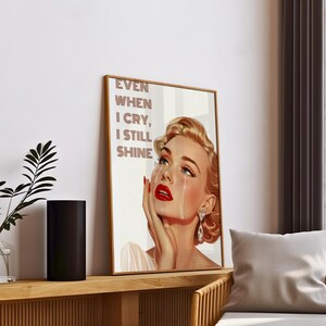 May include: A vintage-style poster featuring a woman with blonde hair and red lipstick crying. The text on the poster reads "Even when I cry, I still shine."