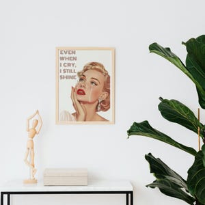 May include: A vintage-style poster featuring a woman with blonde hair and red lipstick crying. The text on the poster reads "Even when I cry, I still shine."