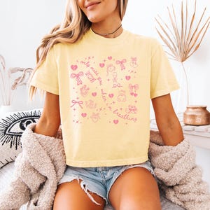 Pode incluir: Camiseta amarelo claro com ilustra&ccedil;&otilde;es gr&aacute;ficas rosa e o texto "I only miss you when I'm breathing". O design inclui cora&ccedil;&otilde;es, la&ccedil;os e outros s&iacute;mbolos fofos. A camiseta &eacute; um estilo casual e confort&aacute;vel.