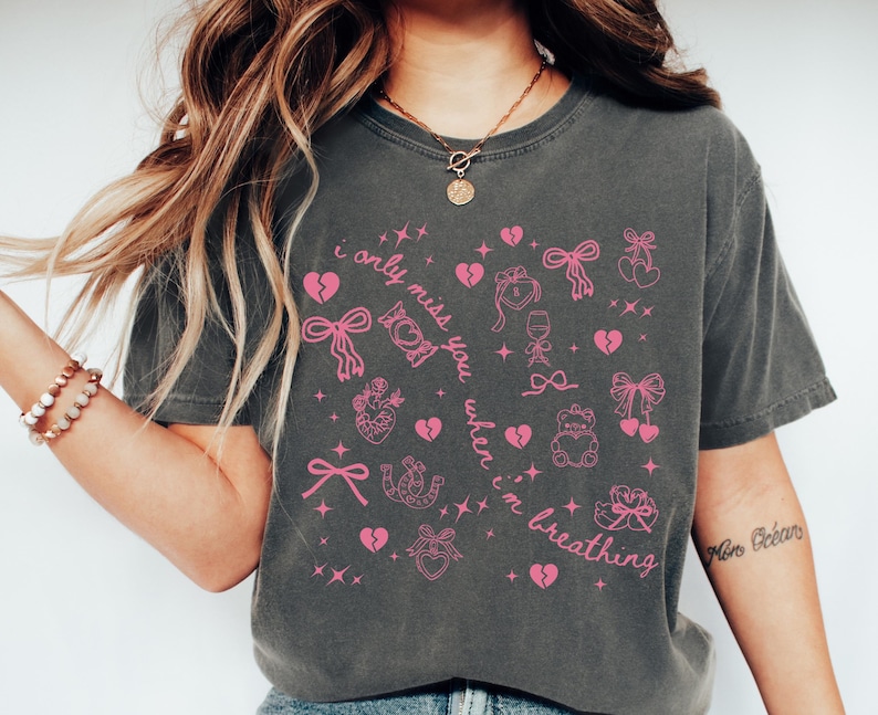 May include: Dark gray t-shirt with pink graphic elements and text. The design includes hearts, bows, and the phrase "i only miss you when i'm breathing". The shirt has a vintage, worn look.