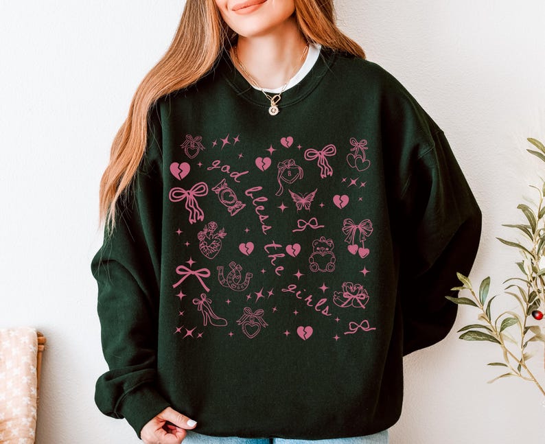 Może przedstawiać: Ciemnozielona bluza z białym kołnierzem, z r&oacute;żowym wzorem graficznym. Wz&oacute;r zawiera kokardy, serca, motyle i napis "god bless the girls". Swobodny, wygodny top.