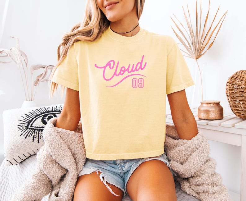 Puede incluir: Camiseta amarilla clara con la inscripci&oacute;n rosa "Cloud 09". La parte superior de manga corta se usa con pantalones cortos de mezclilla y un su&eacute;ter beige. El dise&ntilde;o es simple y casual.