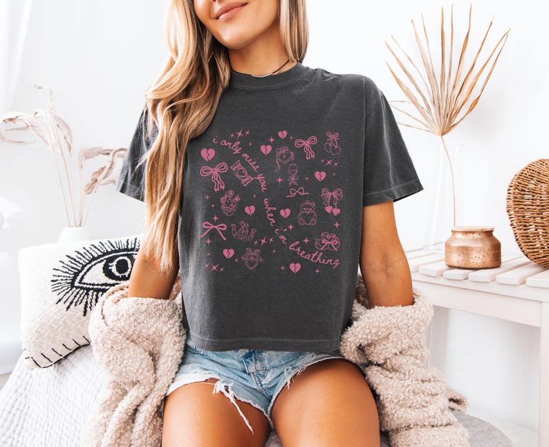 Pode incluir: T-shirt cinza escuro com um design gr&aacute;fico rosa com cora&ccedil;&otilde;es, la&ccedil;os e o texto "I only miss you when I'm breathing". A camisa &eacute; um estilo casual e confort&aacute;vel.