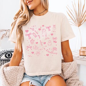 Pode incluir: Camiseta creme com um design gr&aacute;fico rosa. O design inclui cora&ccedil;&otilde;es, la&ccedil;os e o texto "I only miss you when I'm breathing". A camisa &eacute; de estilo casual.