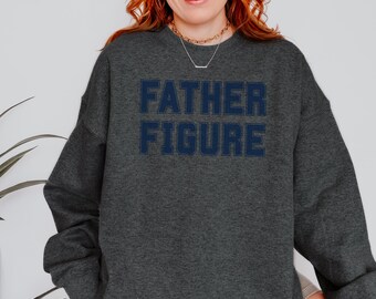 May include: Dark gray sweatshirt with the words "FATHER FIGURE" in navy blue block letters. The sweatshirt has a crew neck and long sleeves. The text is centered on the chest.