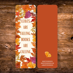 May include: A rectangular bookmark with a cream-colored front featuring a border of watercolor autumn leaves and the text "LEAVES ARE FALLING, BOOKS ARE CALLING". The back is solid burnt orange with a single leaf and the text "MIGHTYPENDESIGNS".