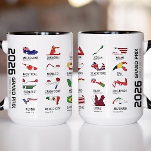 May include: White ceramic mug with a black handle and rim, featuring the 2026 Formula One Grand Prix calendar. The mug displays race locations with flags and track layouts, including Melbourne, Shanghai, and Miami.