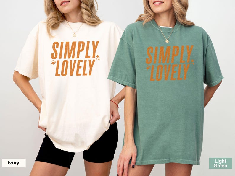 May include: Two oversized t-shirts, one ivory and one light green, each with the text "SIMPLY LOVELY" in orange. The ivory shirt is paired with black shorts. The light green shirt is paired with a necklace.