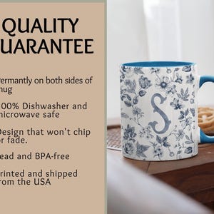 Peut inclure: Tasse en c&eacute;ramique blanche avec int&eacute;rieur et anse bleus. La tasse pr&eacute;sente un motif floral bleu et blanc, avec la lettre "S" au centre. Le texte "QUALITY GUARANTEE" est visible sur le c&ocirc;t&eacute; gauche de l'image.