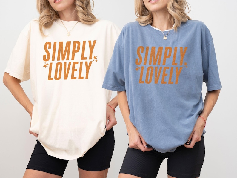 May include: Two oversized t-shirts, one cream and one blue, each with the text "SIMPLY LOVELY" in orange. The shirts are paired with black shorts. The image showcases casual, comfortable apparel.