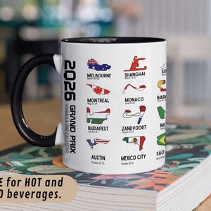 Peut inclure: Mug en c&eacute;ramique blanche avec une anse et un bord noirs, pr&eacute;sentant un calendrier du Grand Prix de Formule 1 2026. La tasse affiche les lieux des courses avec leurs drapeaux et leurs dates. Le texte sur la tasse indique "SAVE for HOT and COLD beverages."